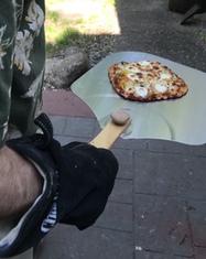 Pizza being placed in outdoor pizza oven.