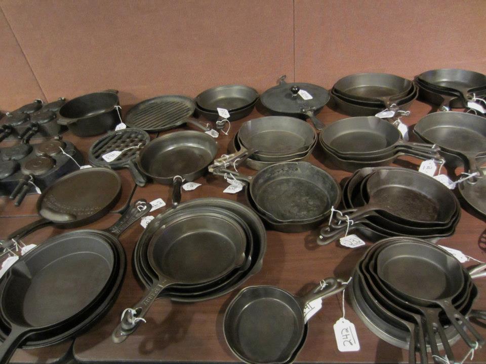 Many vintage and antique cast iron skillets at an auction awaiting inspection. 
