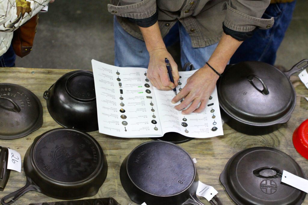 Person making notes in the auction catalog about a piece of vintage or antique cast iron cookware that he had recently previewed before the auction began. 