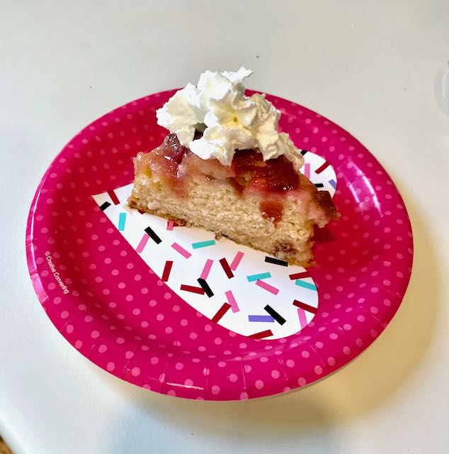 Slice of rhubarb upside down cake with whipped cream on paper plate. 