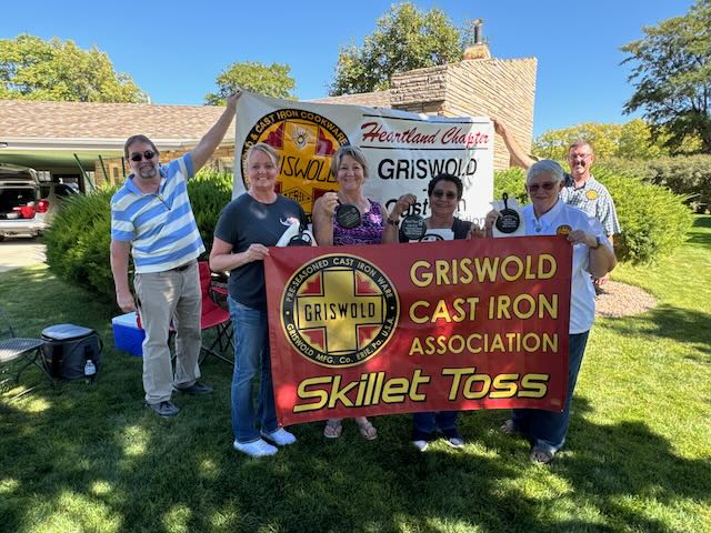 Winners of the skillet toss in front of the Heartland Chapter sign, holding the Griswold cast iron associatiobn skillet toss sign. 