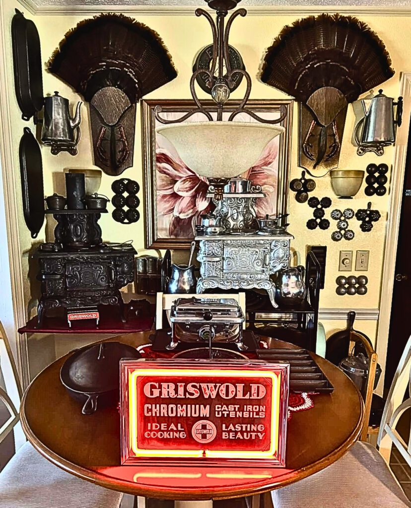 Display of vintage and antique cast iron in Gary Taylor's home, including Favorite silver-plated stove and Griswold neon lit sign. 
