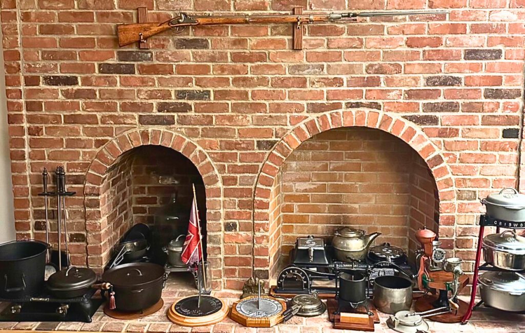 Plated and black antique cast iron on fireplace hearth including Griswold sun dials, dutch ovens, tea pots. 