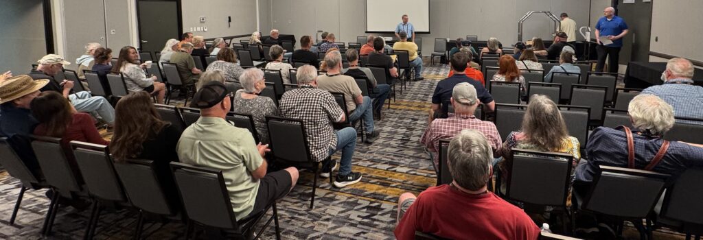 Ballroom with many people seated listening to speaker at the cast iron convention. 