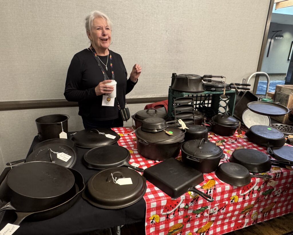 lady at table with many pieces of vintage cast iron cookware at the cast iron convention. 