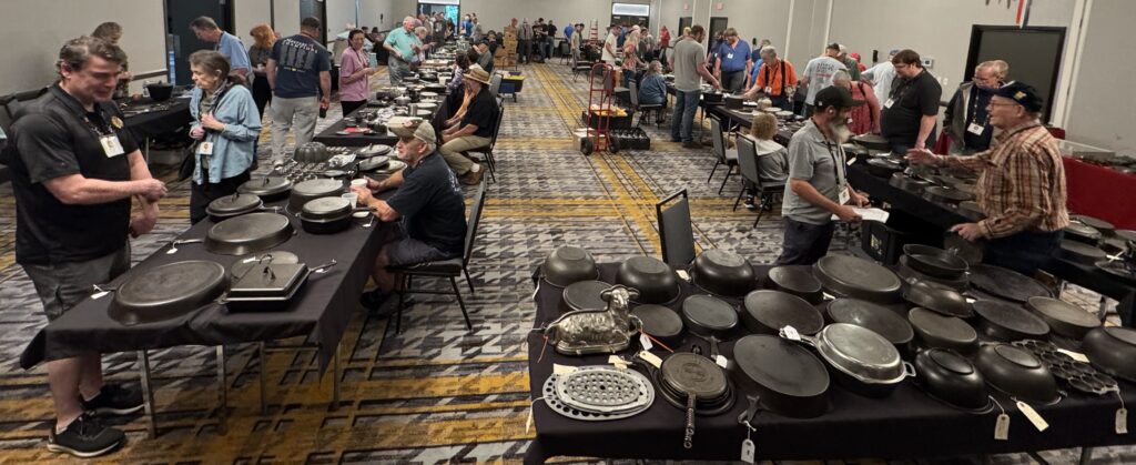 Large room with many tables filled with pieces of vintage and antique cast iron cookware for sale at the cast iron convention. 