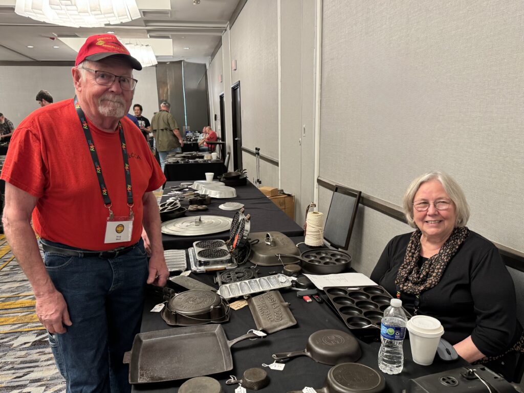 Doug and Kathy Wenz at table with many pieces of vintage cast iron cookware at the cast iron convention. 