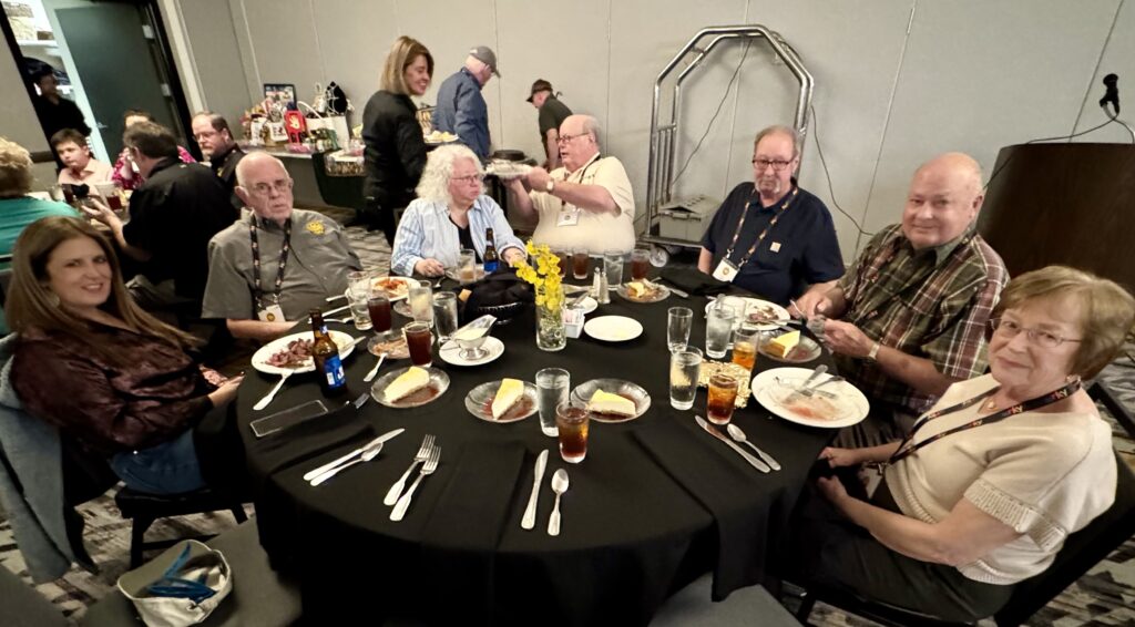 Cast iron convention attendees at a round table eating dessert. 