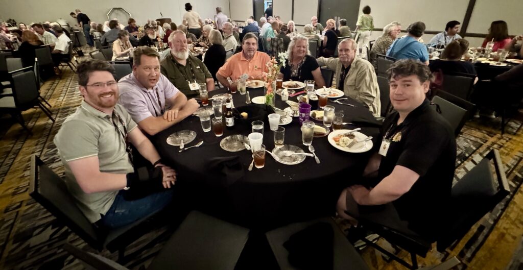 Castt iron convention attendees at a round table eating dinner in a banquet room. 