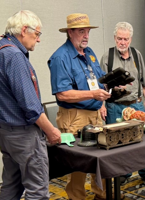 3 men at a table looking at and talking about a piece of vintage cast iron at the cast iron convention 